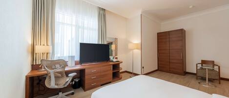 Una camera d'albergo con un letto, una scrivania con computer e sedia, una TV, un armadio e un tavolino con una poltrona.