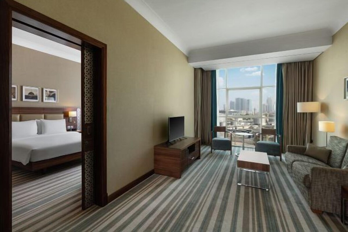 Ein Hotelzimmer mit Bett, Fernseher, Schreibtisch, Stuhl und Blick auf die Stadt.