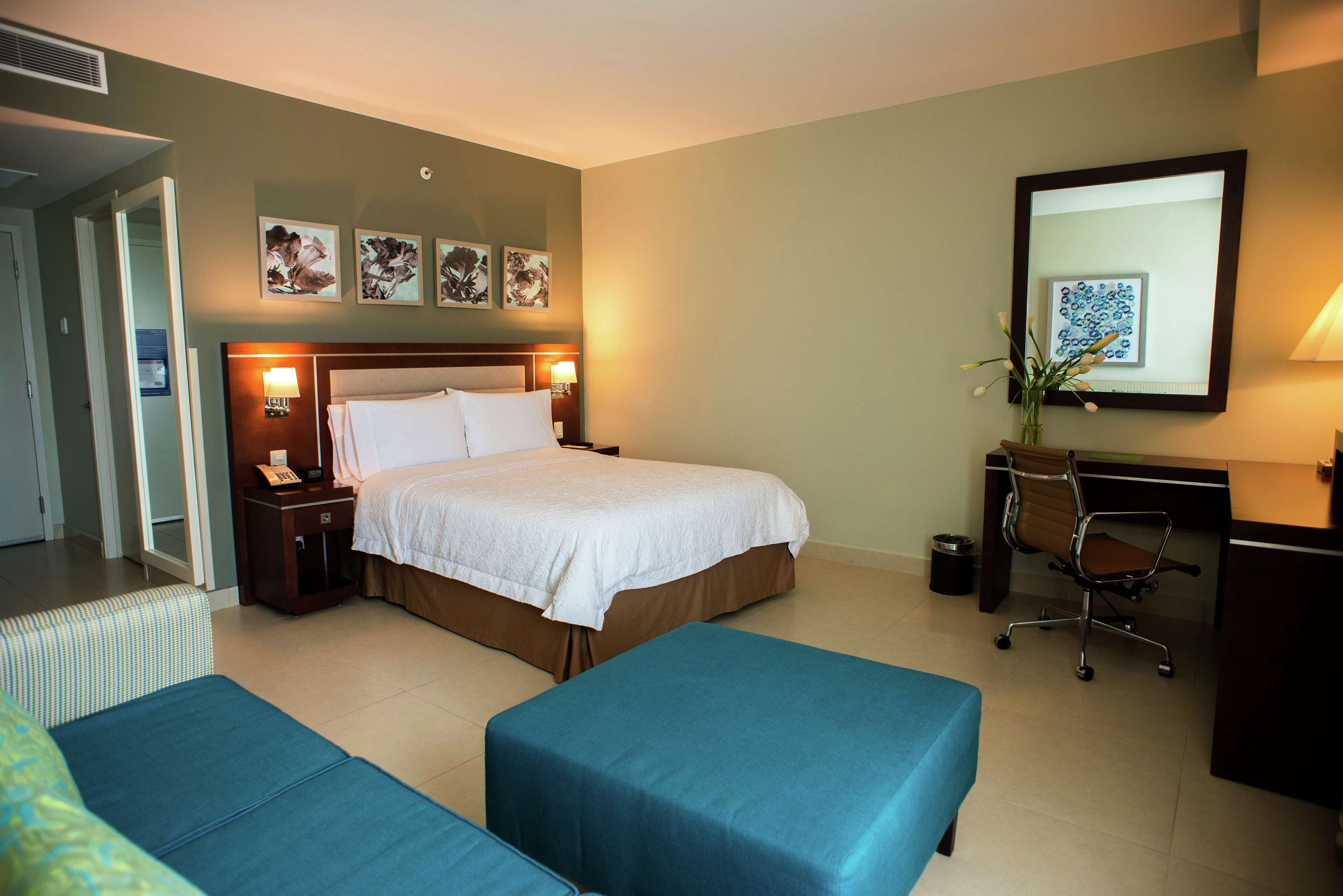 Une chambre d’hôtel avec un lit, deux canapés bleus, un bureau avec une chaise et des œuvres d’art accrochées aux murs.