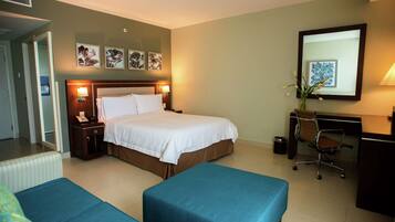 A hotel room with a bed, two blue sofas, a desk with a chair, and artwork on the walls.