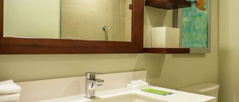 A bathroom with a white sink, a mirror, a toilet, and a shelf with toiletries.