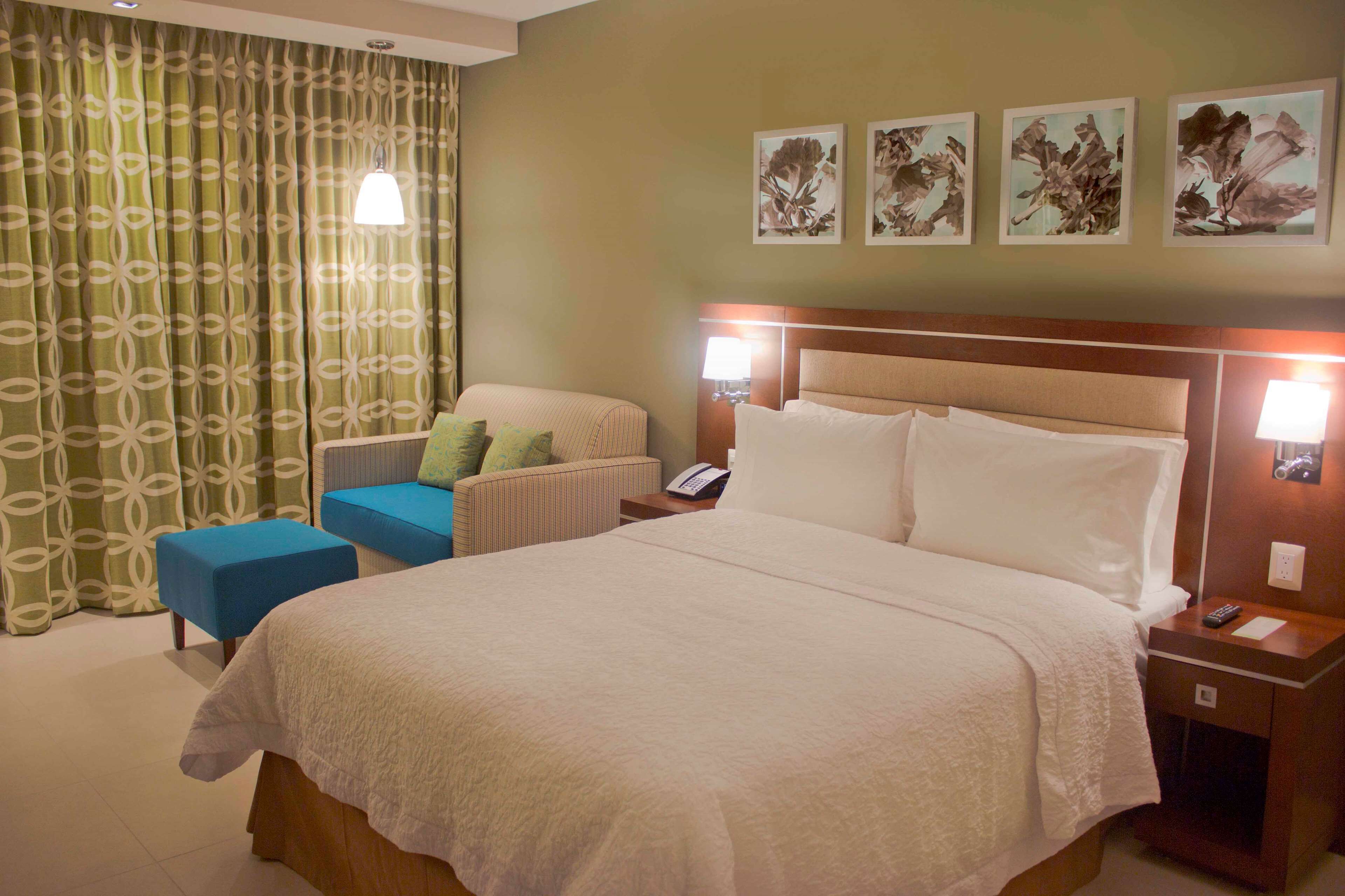 Ein Hotelzimmer mit einem großen Bett, einem Sessel, einem Nachttisch und einer Wand mit gerahmten Kunstwerken.