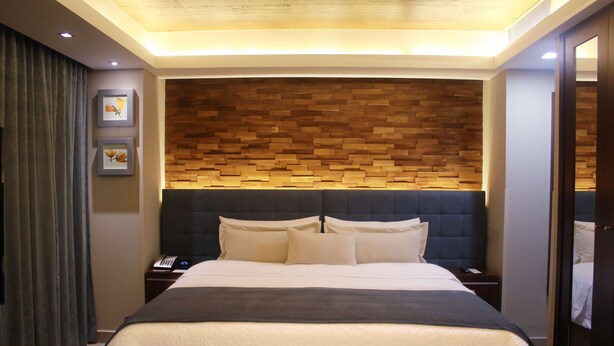 Una habitación de hotel moderna con una cama grande, un cabecero de madera, una mesita de noche y un pequeño escritorio.
