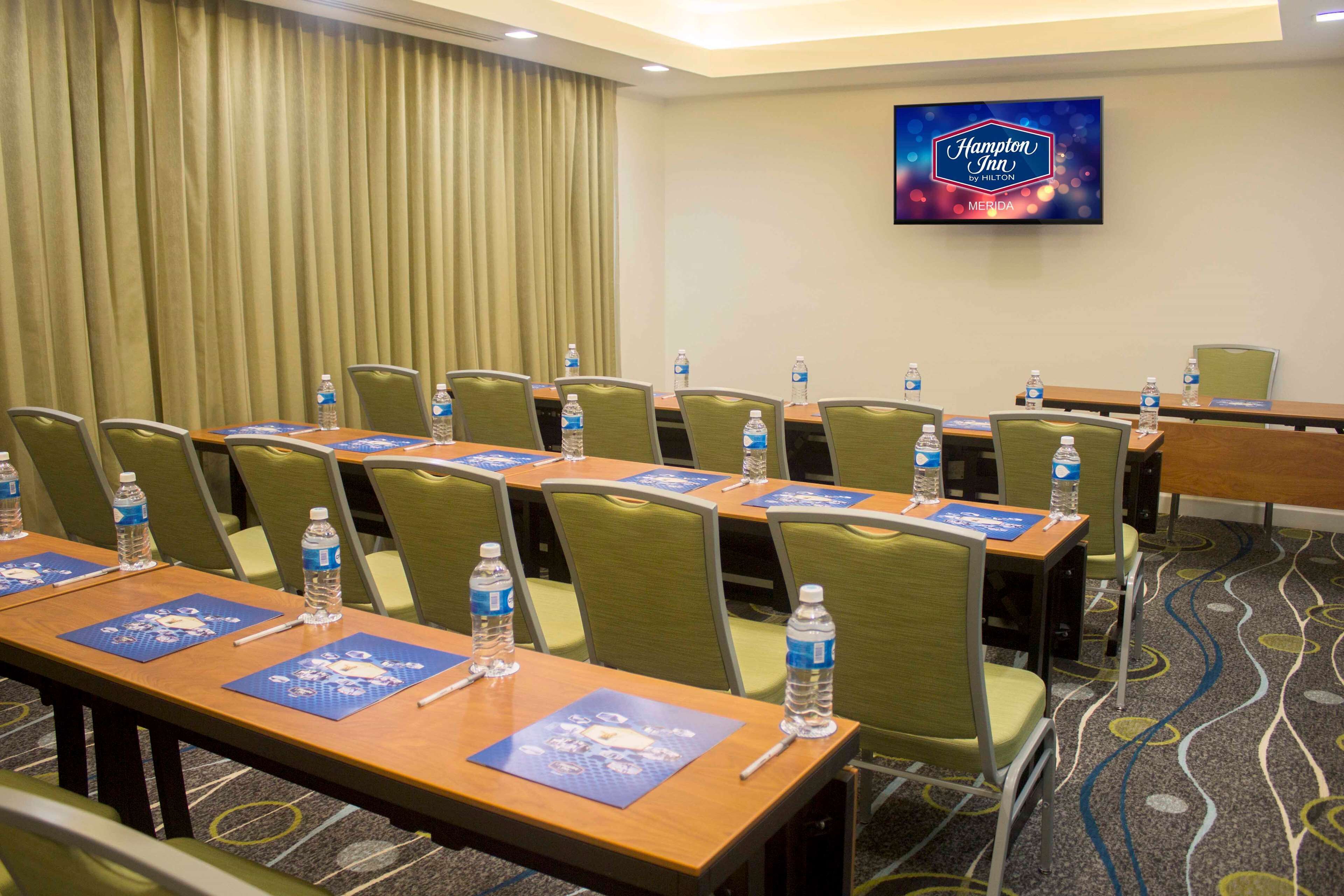 A conference room with multiple tables, chairs, water bottles, nameplates, and a Hampton Inn by Hilton sign.