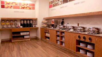 Montaje de bufé con múltiples estaciones de servicio, incluyendo dispensadores de café, una variedad de alimentos y fuentes de servir ordenadas.