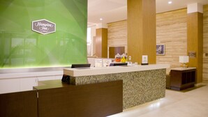 Zona de recepción de hotel con una pared de acento verde, un mostrador de recepción y un panel de pared de madera.