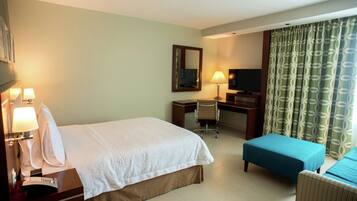 A hotel room with a bed, a desk, a chair, a television, and a window with curtains.