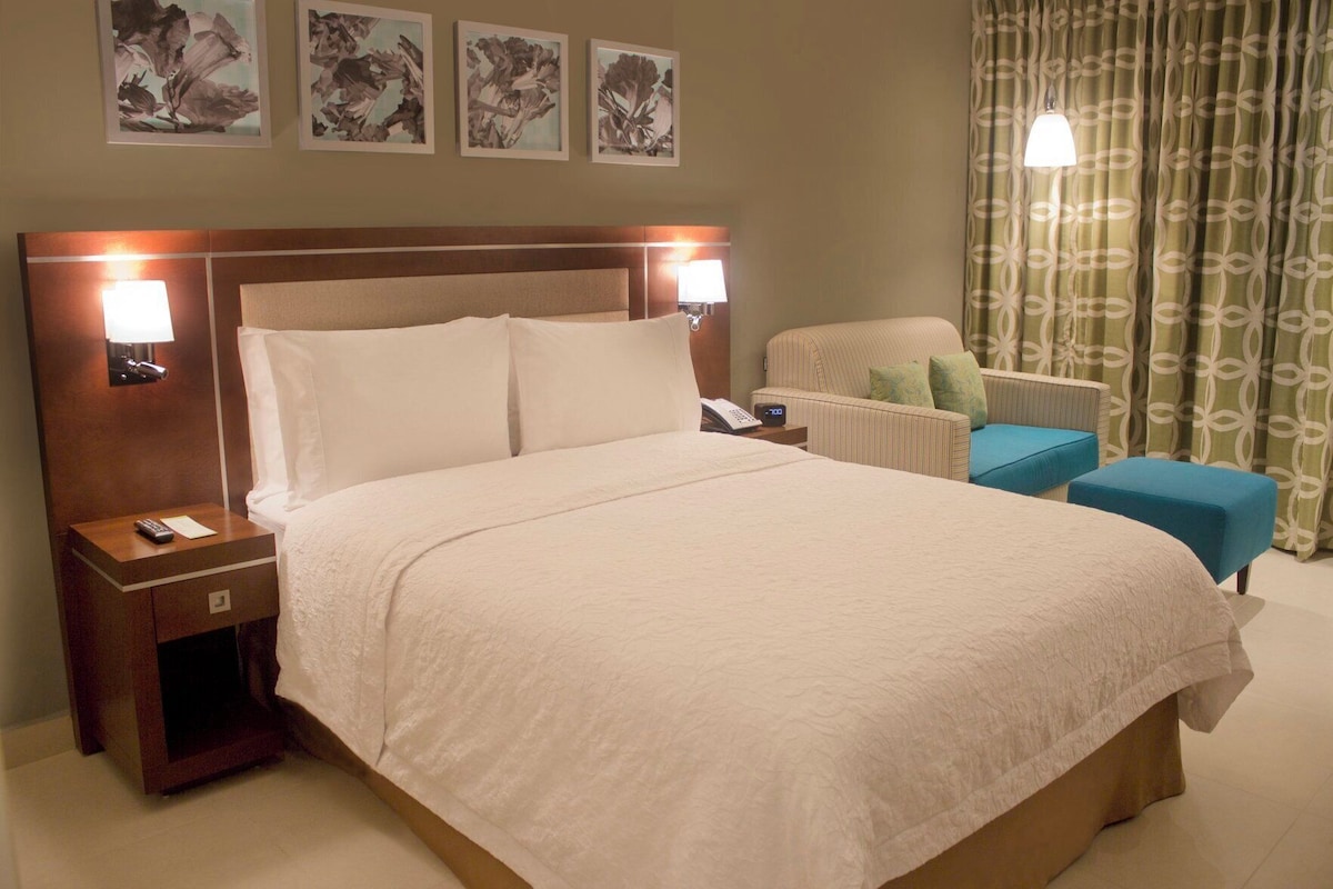 Habitación de hotel con una cama grande, lámparas de noche, una silla y una mesita.