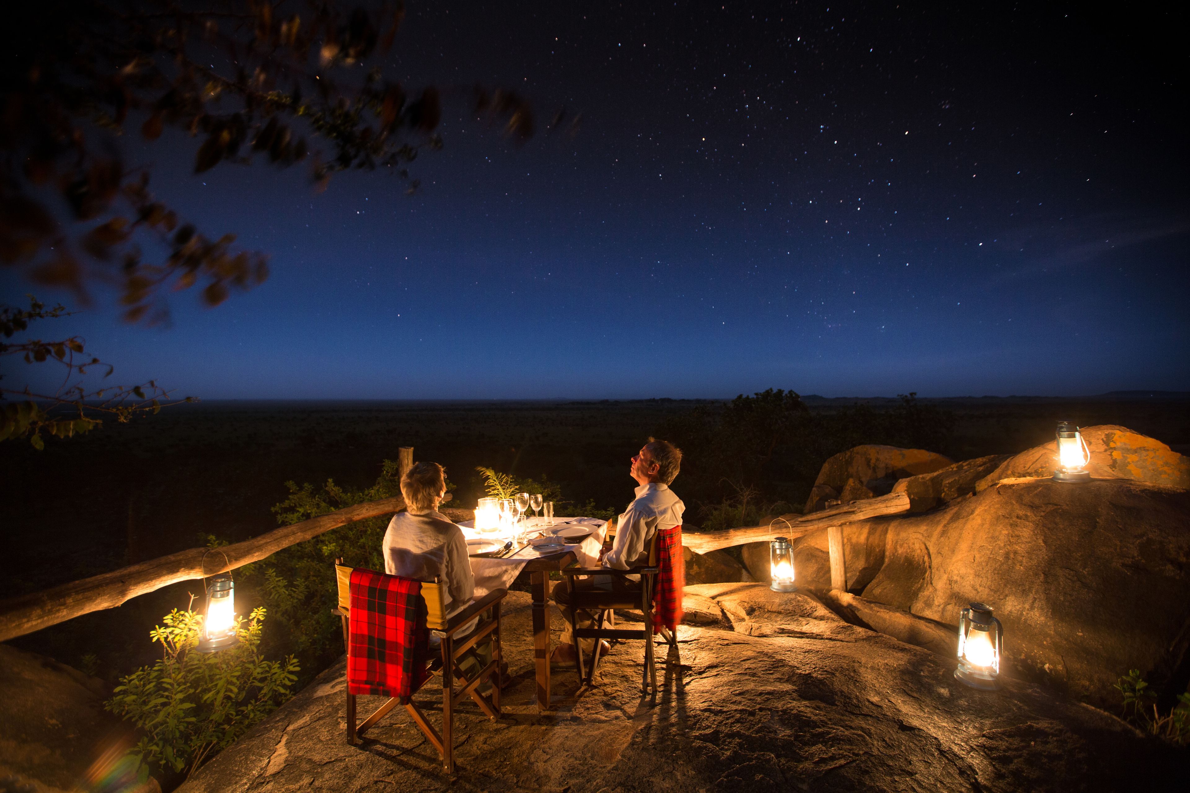Mobiliario para comedor al aire libre con mesa y sillas, rodeado de faroles y con un cielo nocturno estrellado.