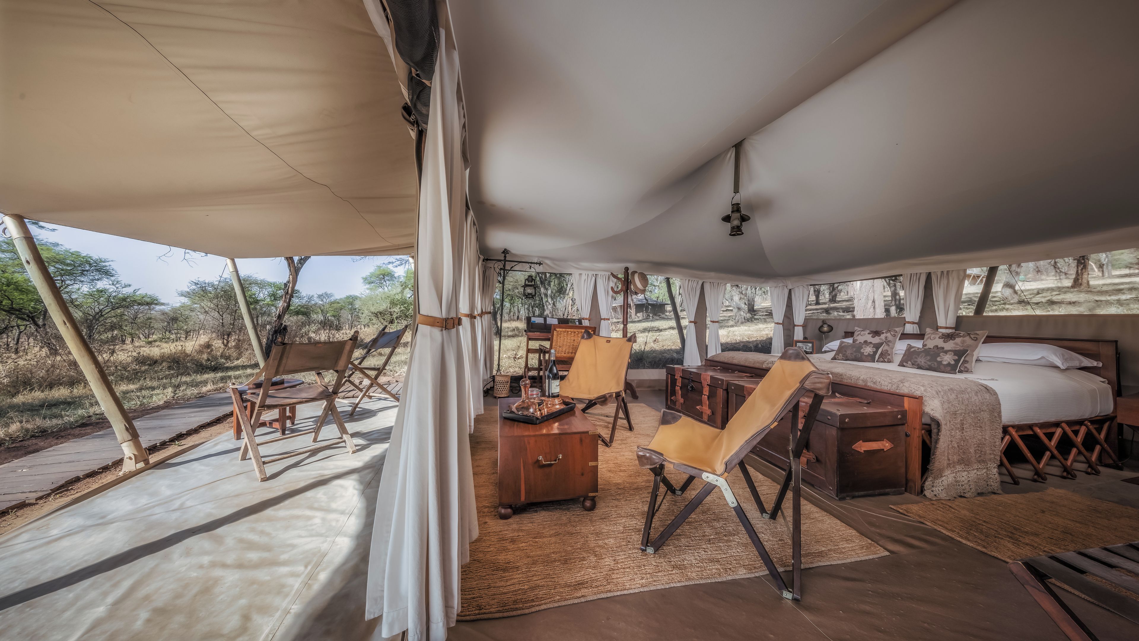A tented accommodation with a bed, seating area, and a view of the outdoors.