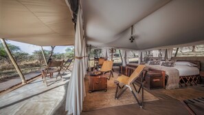 A tented accommodation with a bed, seating area, and a view of the outdoors.