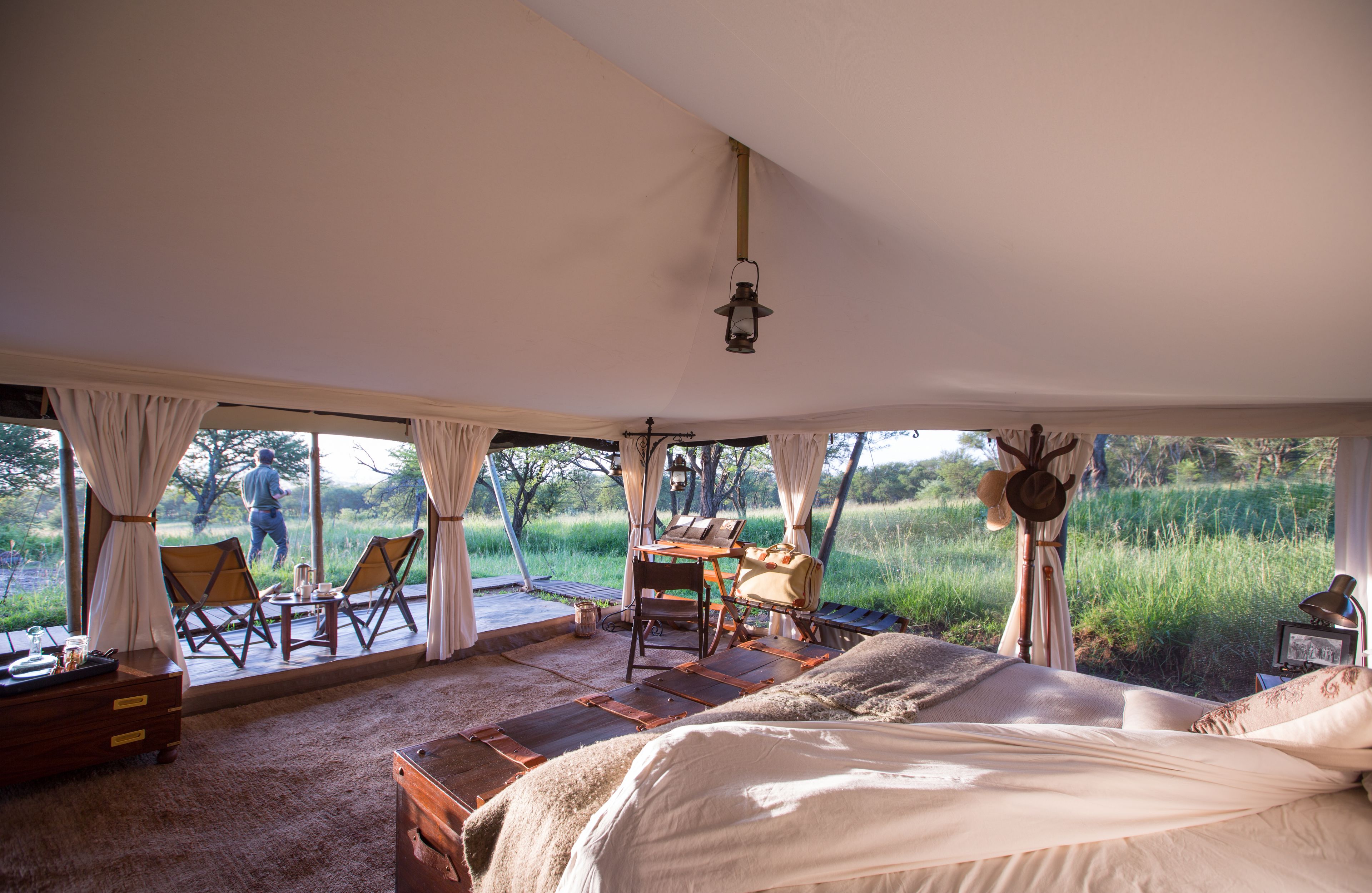 Un dormitorio con una cama grande, un escritorio y dos sillas. Se ve un campo verde a través de las ventanas.