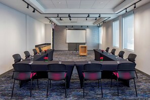 A conference room with a long table, chairs, a projector screen, and a carpeted floor. - Aloft by Marriott Santa Clara (San Jose)