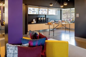 A modern interior with a seating area, a counter with food and drink options, and a menu board. - Aloft by Marriott Santa Clara (San Jose)