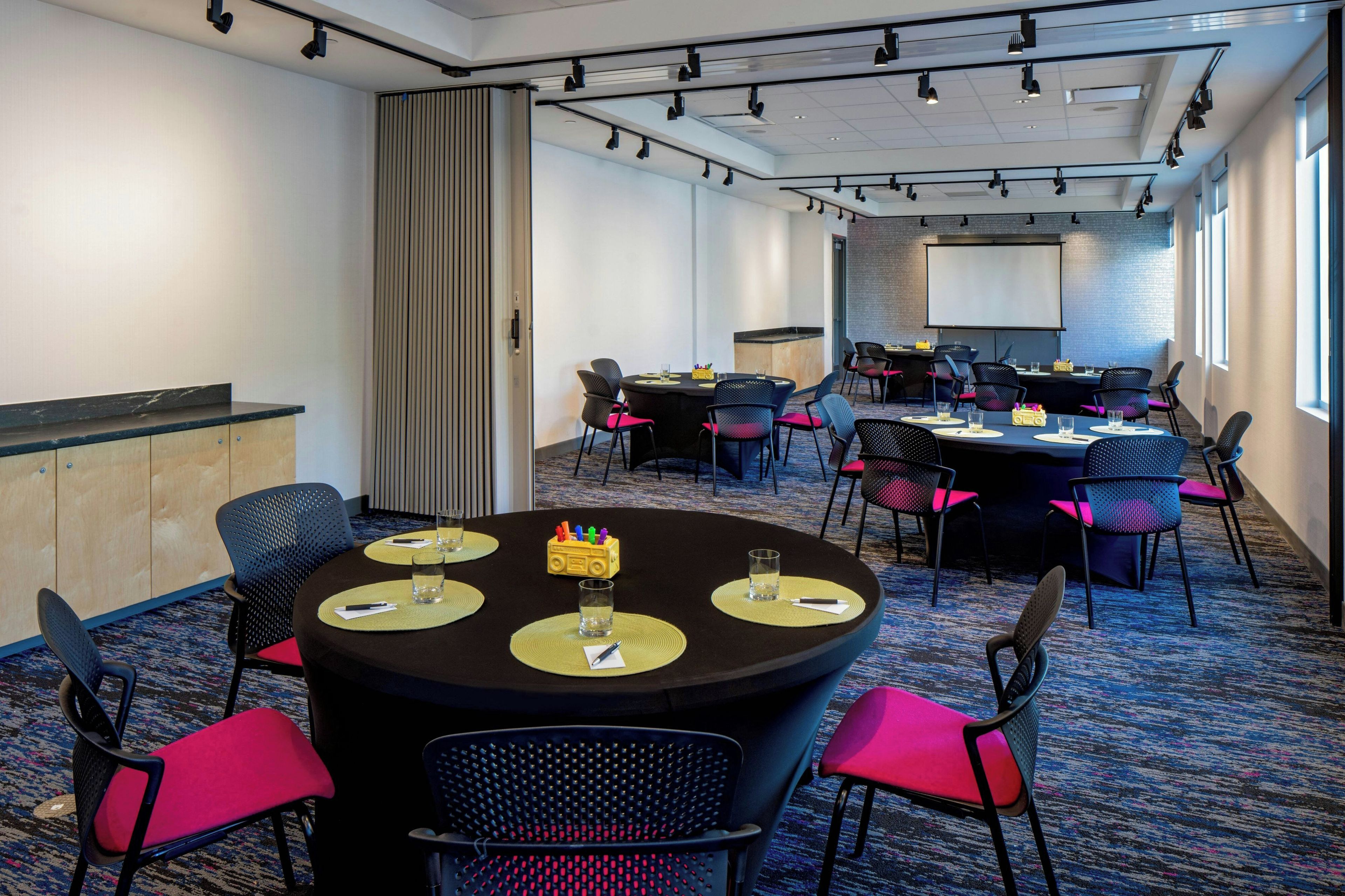 A conference room with round tables, chairs, and a projector screen.