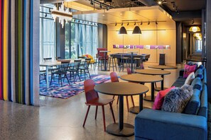 A modern lounge area with round tables, chairs, and a sofa with colorful cushions. - Aloft by Marriott Santa Clara (San Jose)