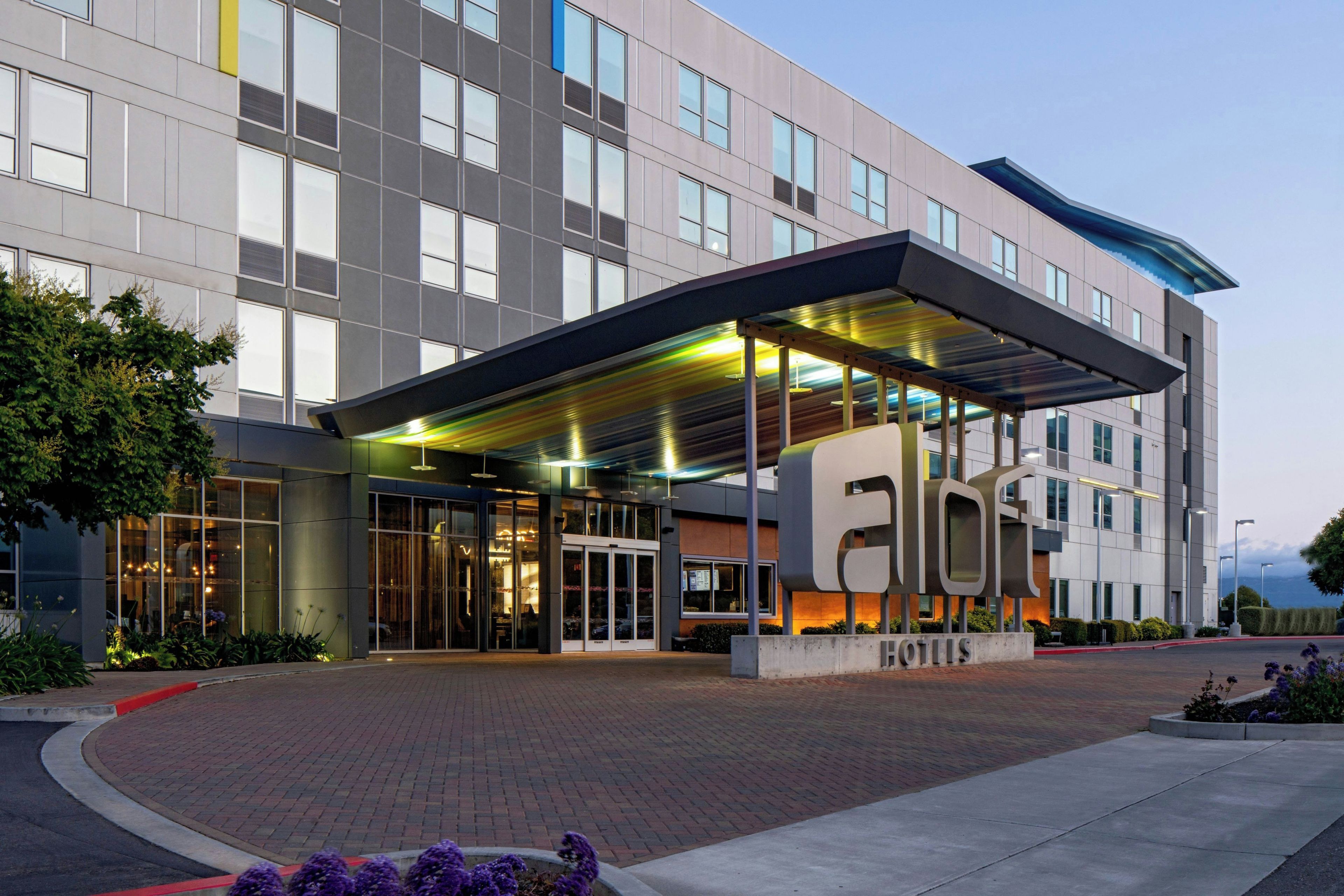 A modern hotel entrance with a covered walkway, glass doors, and a sign indicating the name 'HOTEL'.
