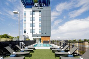 A modern hotel building with a rooftop pool area featuring sun loungers and a clear view of the surrounding landscape. - Aloft by Marriott Santa Clara (San Jose)