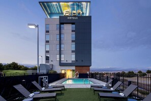 A modern hotel building with a swimming pool and lounge chairs. - Aloft by Marriott Santa Clara (San Jose)
