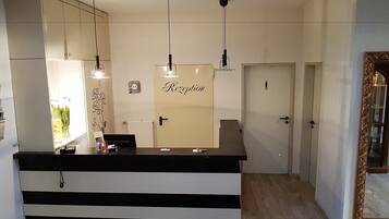 A reception area with a reception desk, three pendant lights, a wall-mounted clock, and a door labeled "Rezeption".