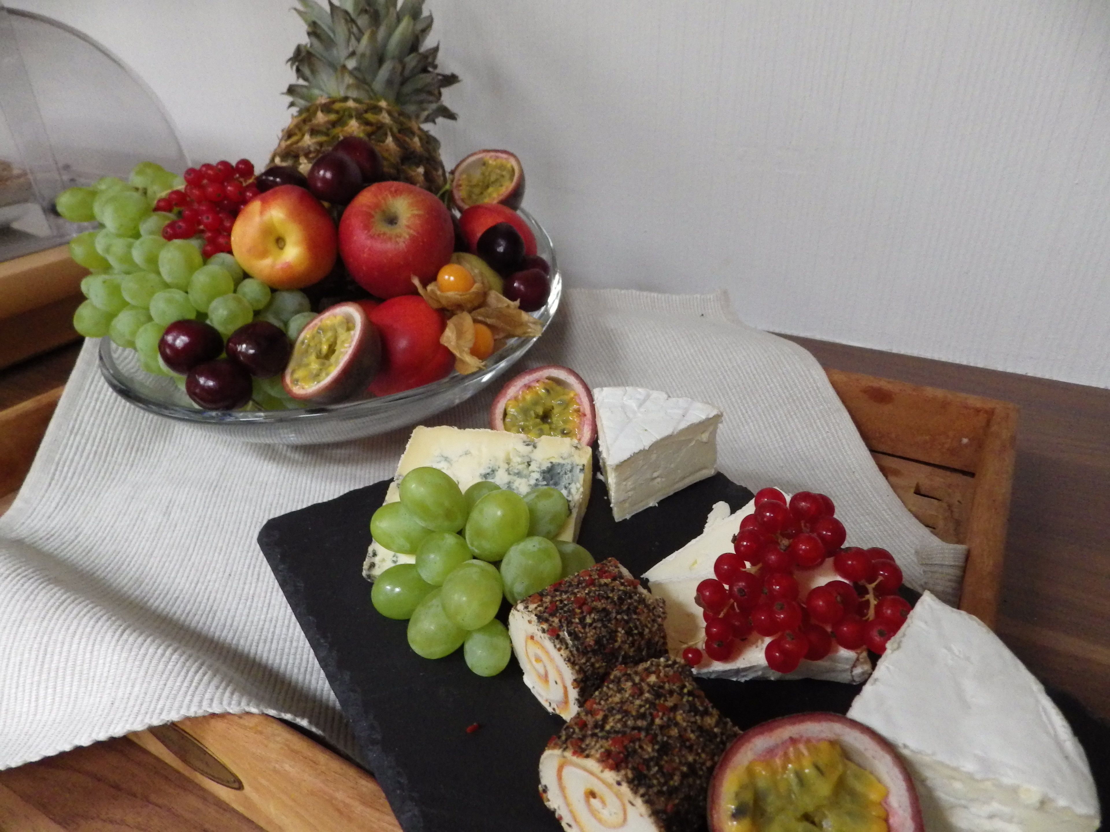 Una tabla de quesos y frutas sobre una mesa de madera con un mantel blanco.