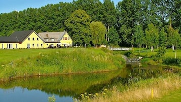 A yellow building with a pond in front, surrounded by greenery and trees.