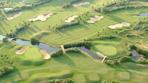 An aerial view of a golf course with multiple bunkers, water hazards, and a forested area in the background. - Pension Haus Heitzig (Lippstadt)
