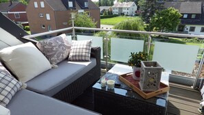 A balcony with a wicker sofa, cushions, a glass table with candles, a tray, and a potted plant. - Pension Haus Heitzig (Lippstadt)