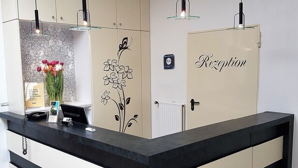 A reception desk with a black and white color scheme, a flower vase, and a sign indicating room number 8.4. - Pension Haus Heitzig (Lippstadt)