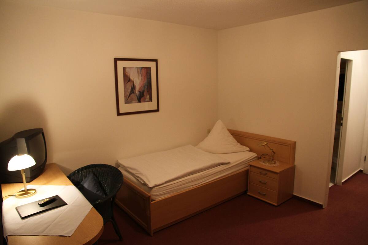 A hotel room with a bed, bedside table, lamp, chair, and a framed picture on the wall.