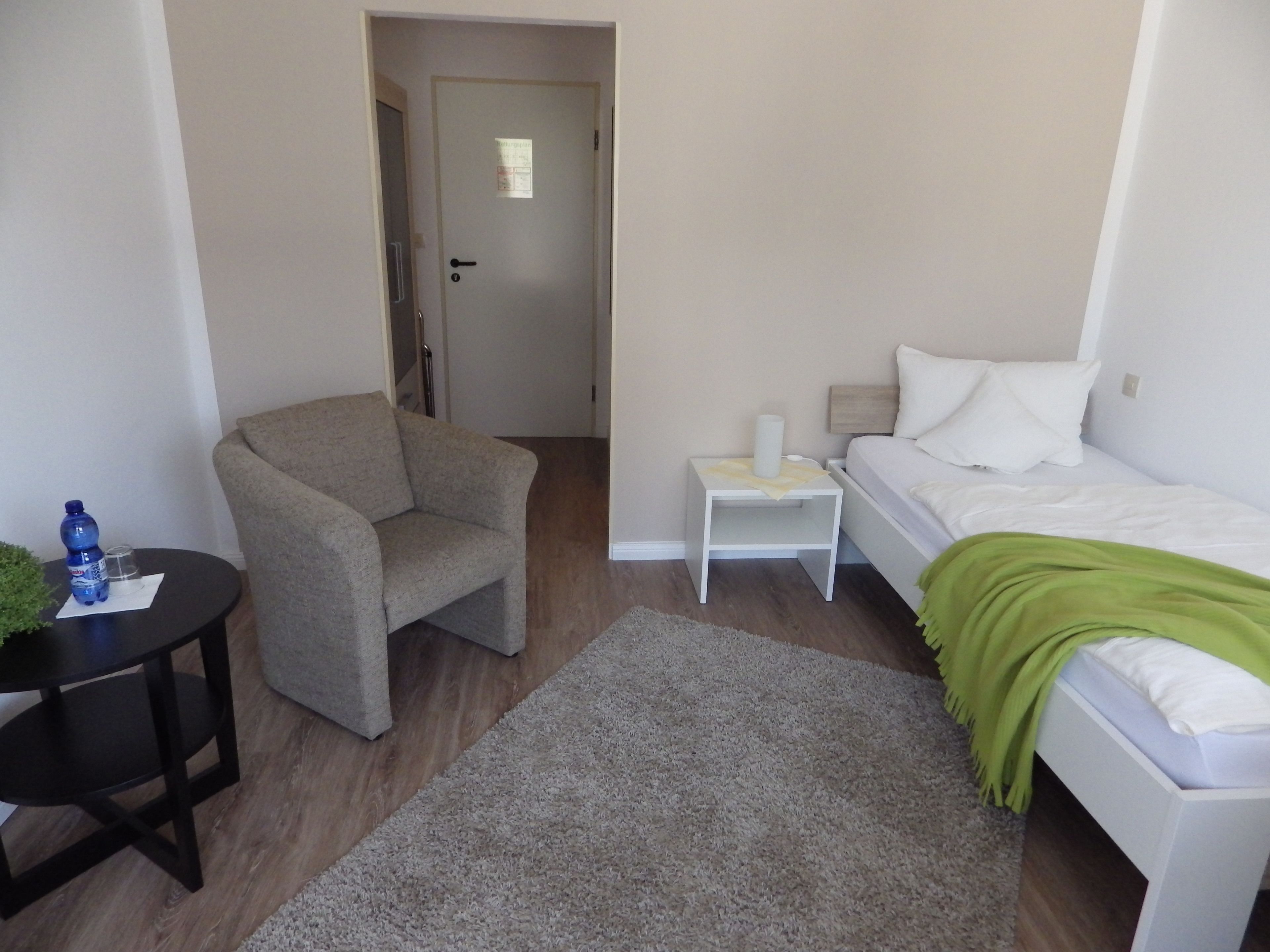 Une chambre à coucher avec un lit, une chaise, une petite table et une porte.