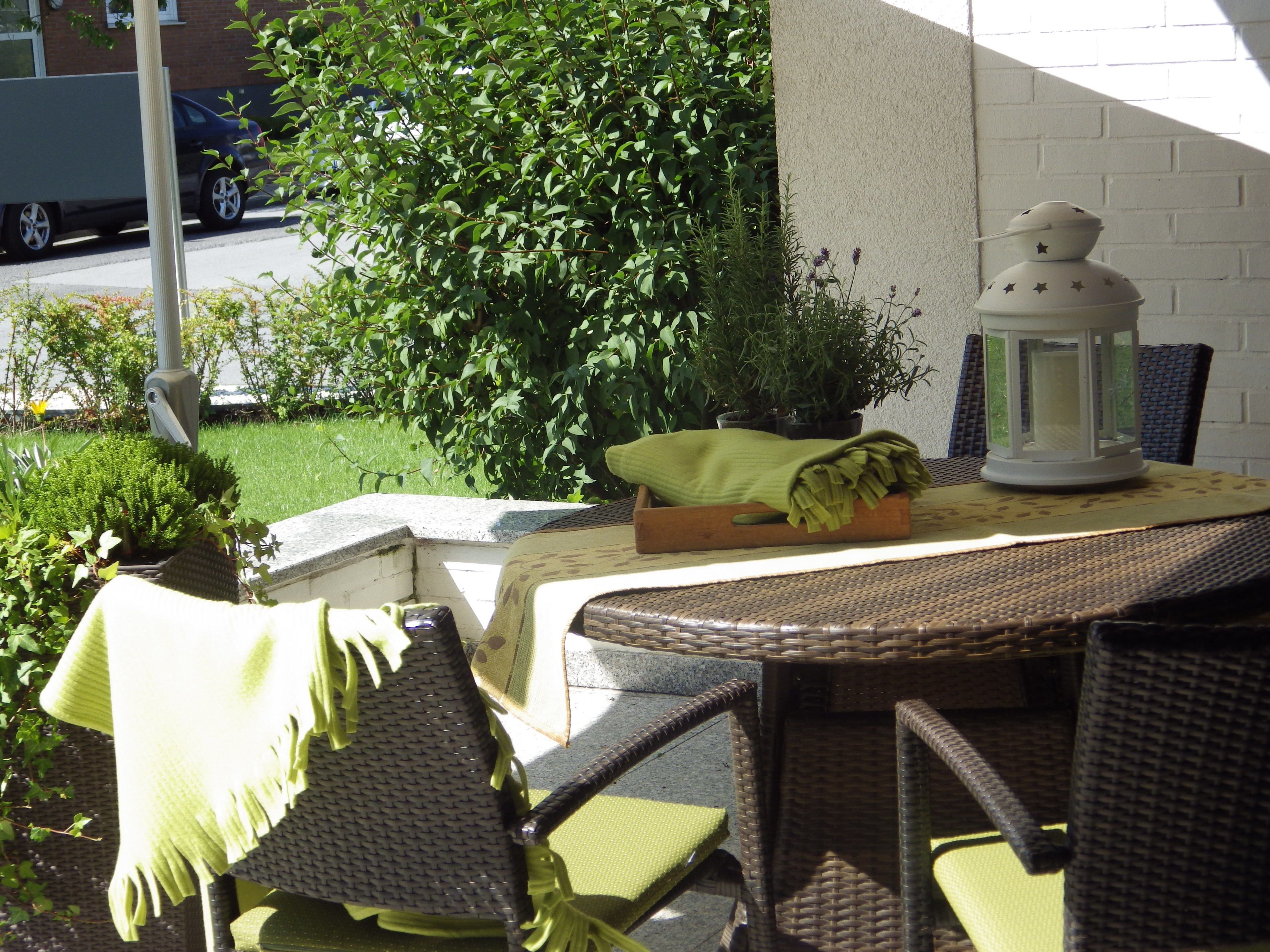 An outdoor patio with wicker furniture, a table with a lantern, and potted plants.