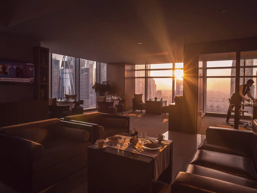 Habitación de hotel moderna con un amplio ventanal que ofrece vistas a la ciudad, un televisor de pantalla plana en la pared y una zona de comedor con una mesa para dos.