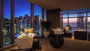 Ein modernes Hotelzimmer mit Blick auf die Stadt, einem Essbereich und einer Sitzecke mit einer großen Pflanze.