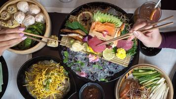 A table with various dishes including dumplings, sashimi, noodles, and a bowl of soup.