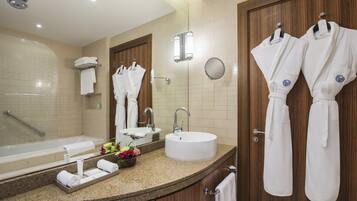 A modern bathroom with a bathtub, sink, and mirror. There are towels and robes hanging on the wall.