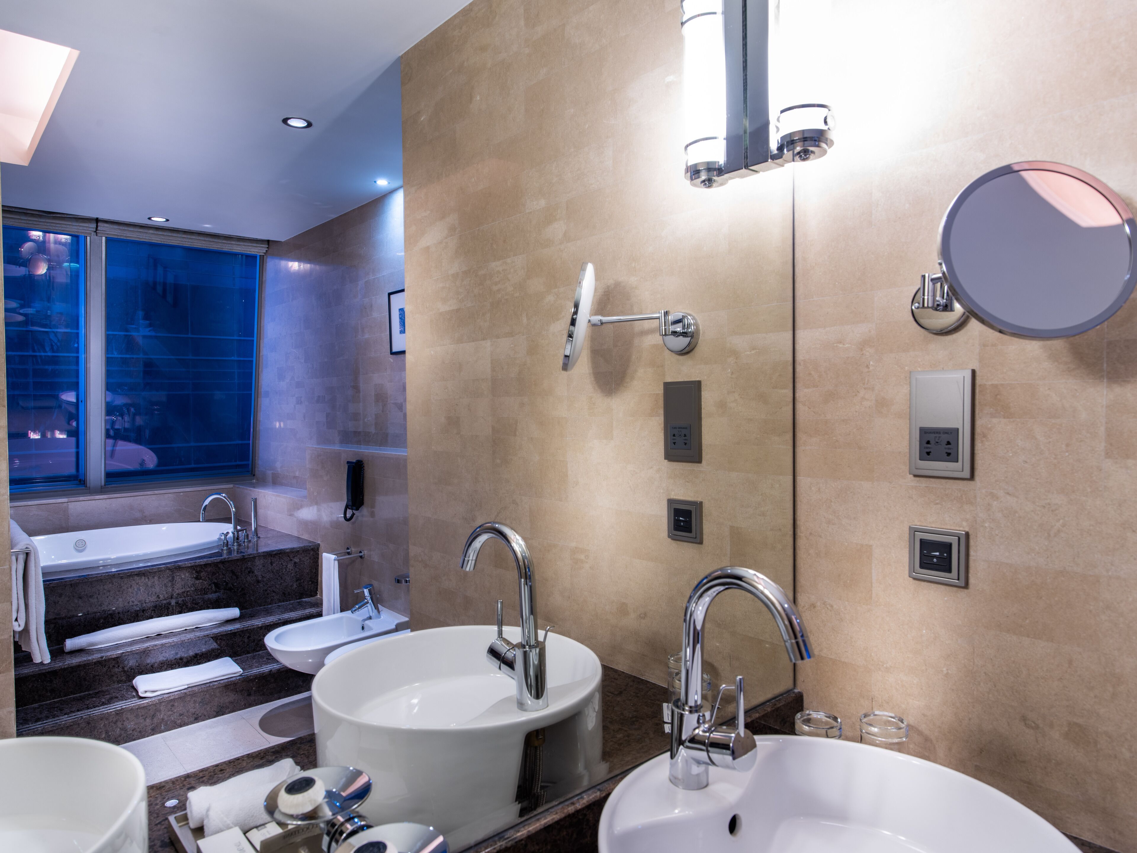 A modern bathroom with a large bathtub, two sinks, and a vanity mirror.