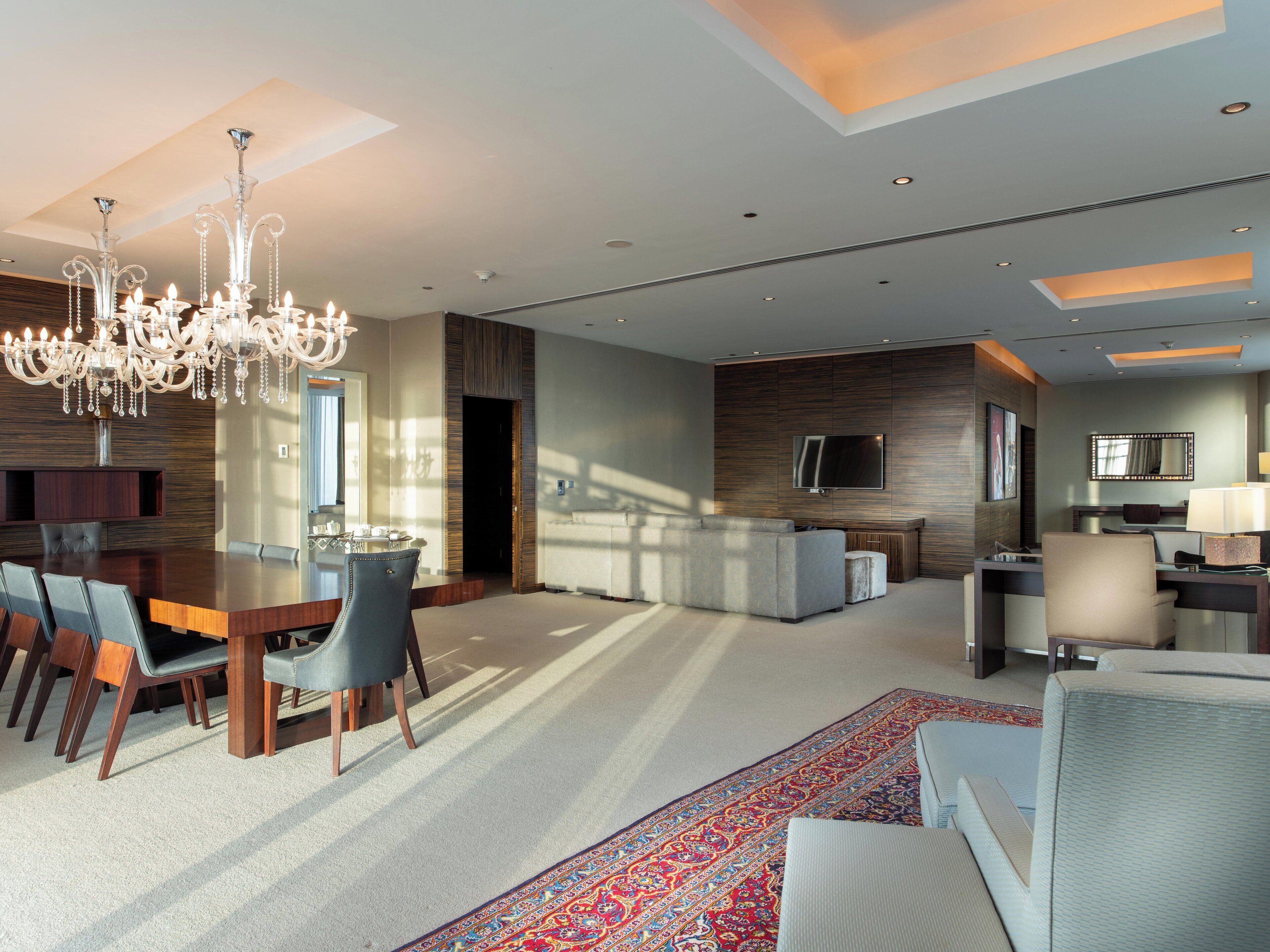 A modern hotel room with a dining area, a sofa, a TV, and a large window.