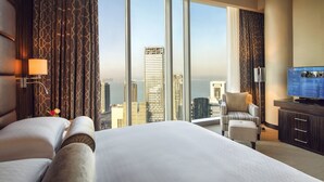 Ein Hotelzimmer mit einem großen Bett, einem Fernseher, einem Sessel und Blick auf die Stadt.