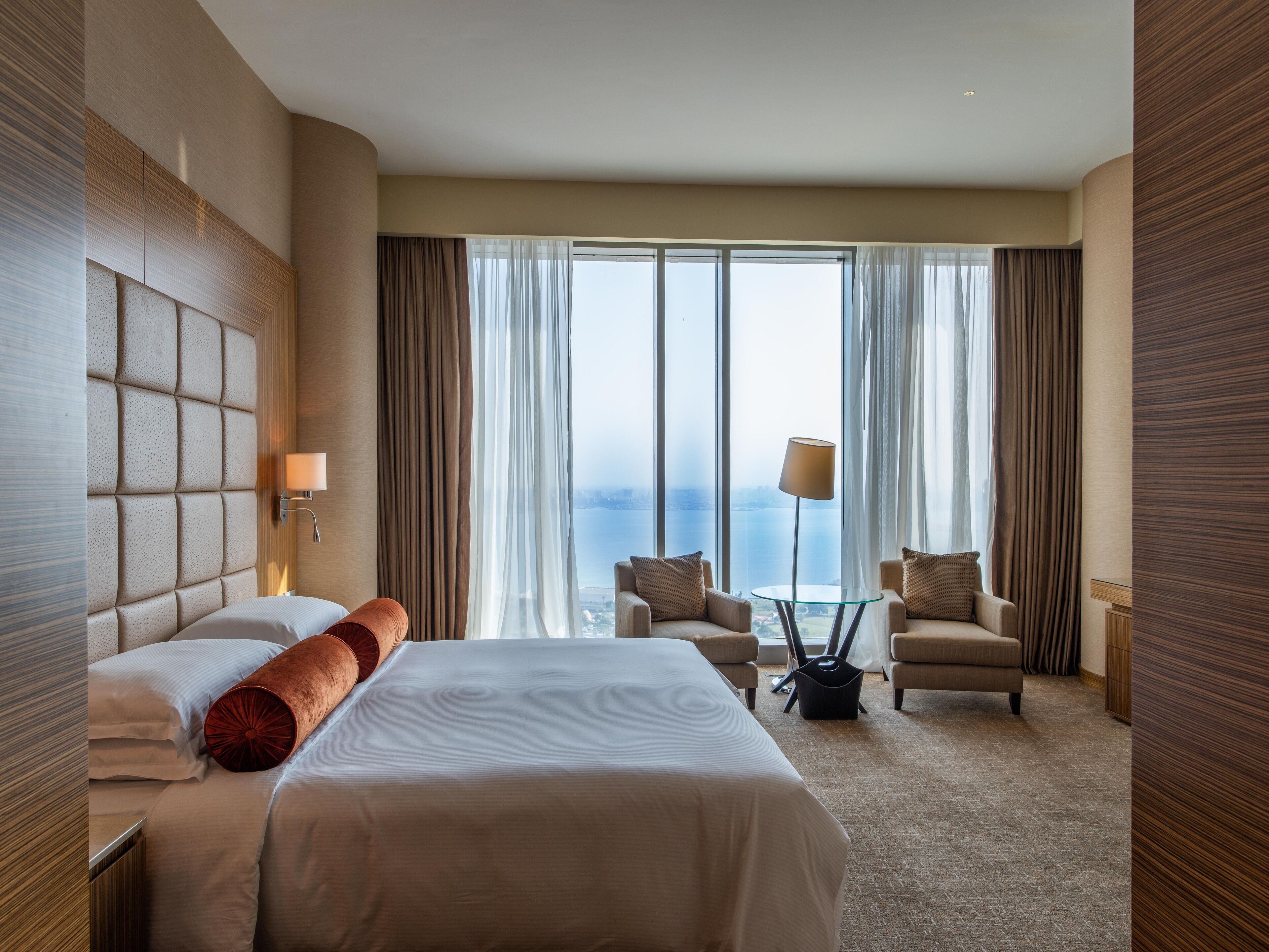 Habitación de hotel con una cama grande, dos sillones, una mesita y vistas al mar a través de amplios ventanales.