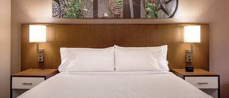 A hotel room with a large bed, two bedside tables, a nightstand with a clock, and a wall-mounted artwork above the bed.