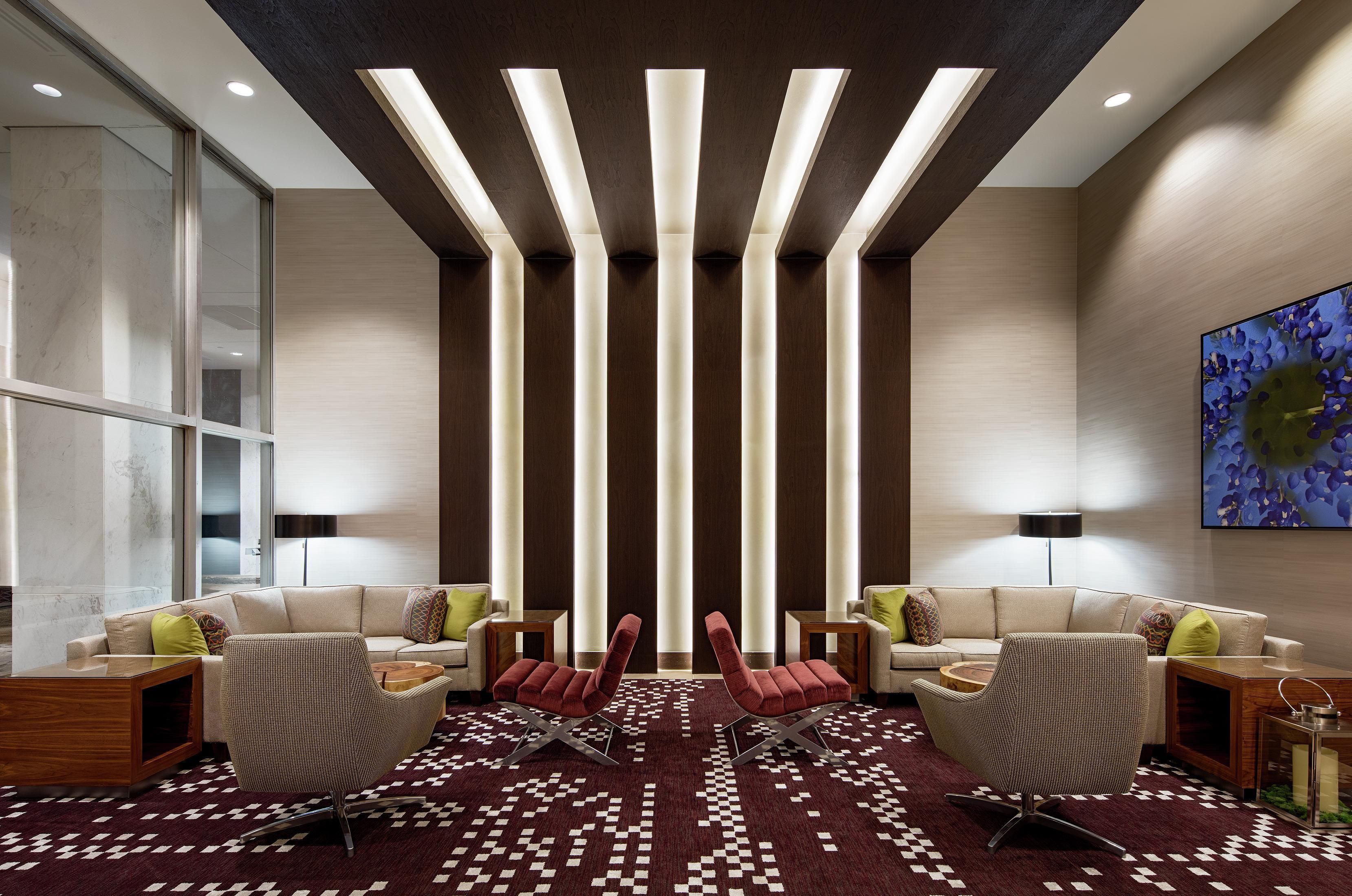 Eine moderne Lobby mit einem Schachbrettmuster-Teppich, zwei Sofas, einem roten Sessel und einem an der Wand montierten Fernseher.