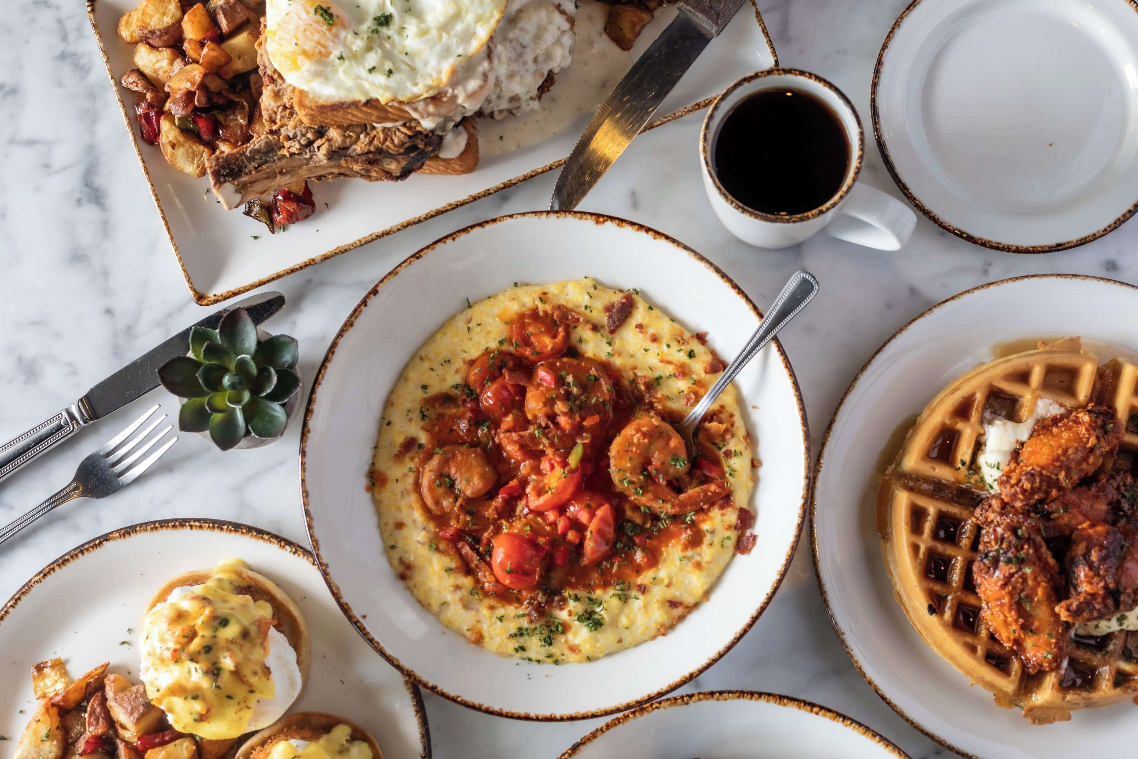 A breakfast spread with various dishes including waffles, scrambled eggs, and a bowl of soup.