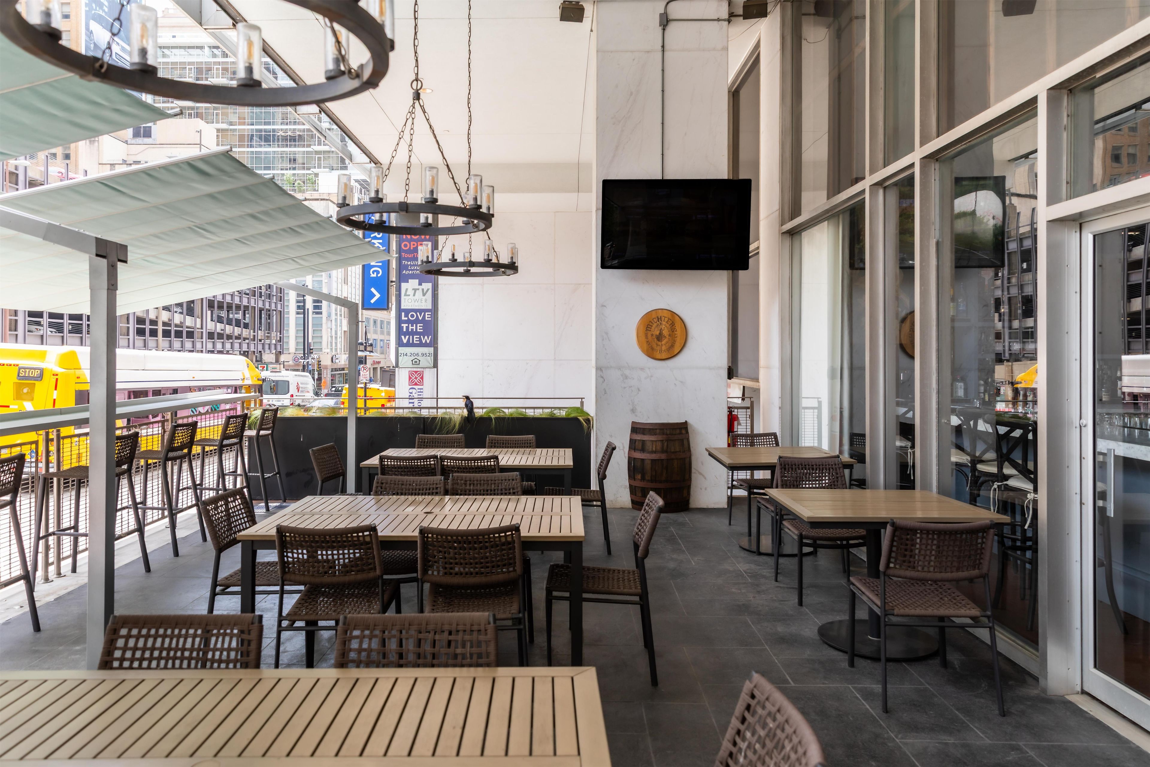 An outdoor dining area with tables and chairs, a mounted television, and a view of the cityscape.