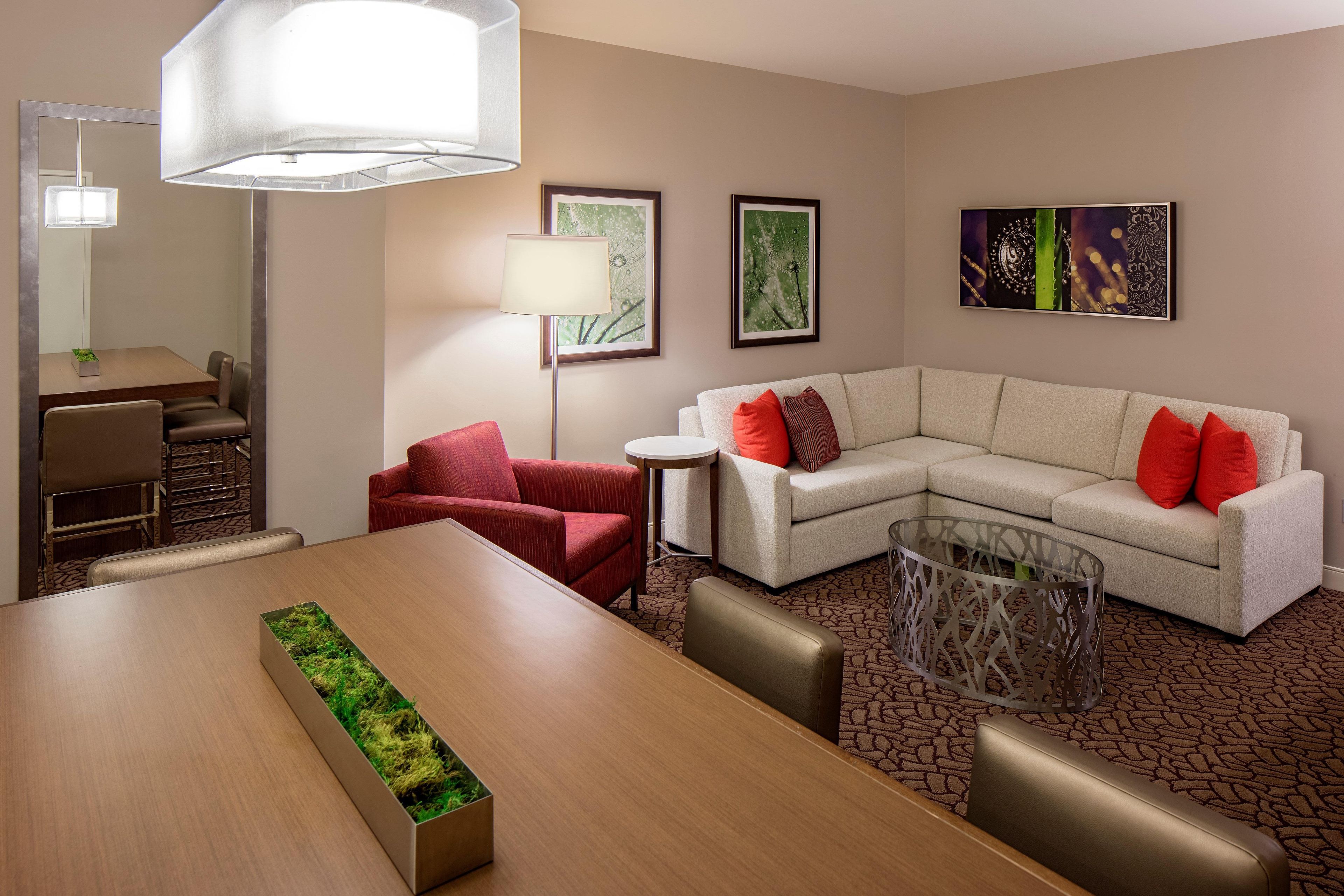 A modern hotel room with a dining area, a sofa set, a side table, and a decorative lamp.