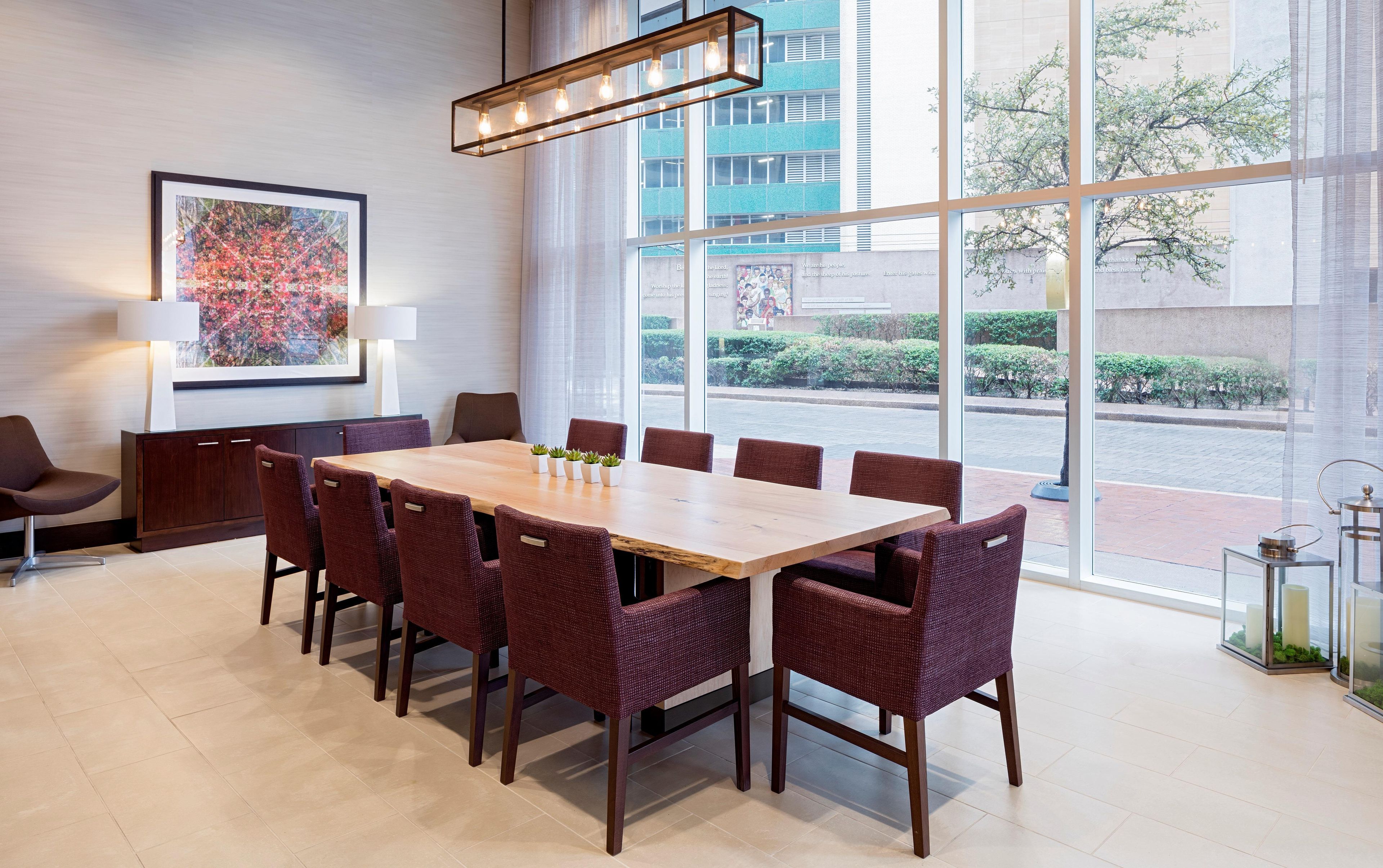 A conference room with a large table and chairs, a framed picture on the wall, and a view of the street through large windows.