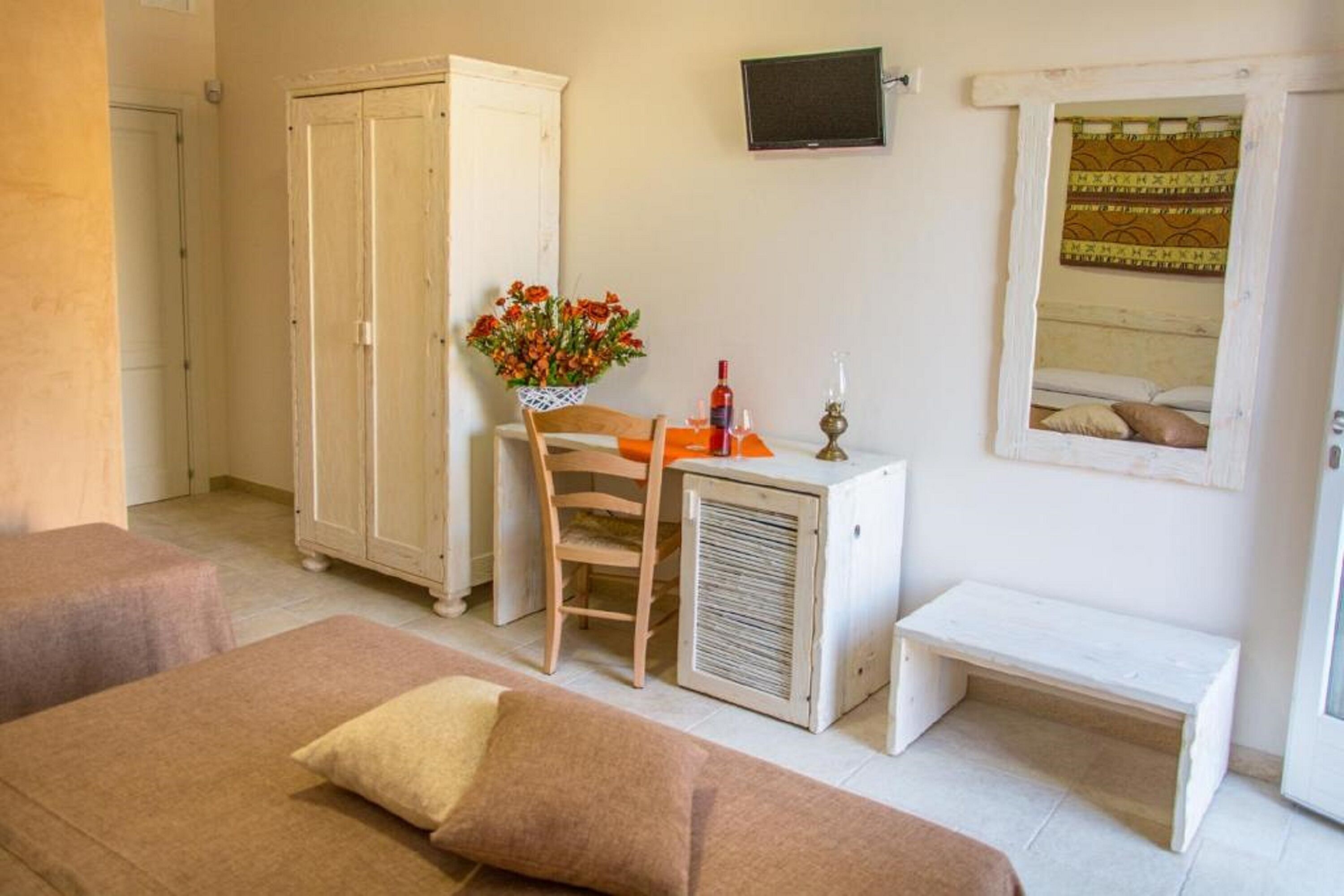 Ein Zimmer mit einem Bett, einem kleinen Tisch mit Blumenvase, einem Sessel, einem Kleiderschrank und einem an der Wand befestigten Fernseher.