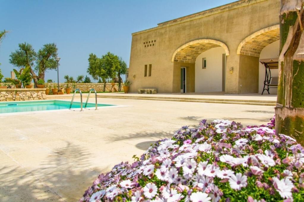 A pool area with a stone wall, a building with arches, and a flower bed.