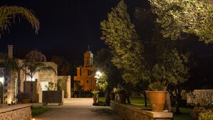 A nighttime view of a courtyard with a pathway leading to a building with a bell tower. - Relais Tenuta Campì (Martano)