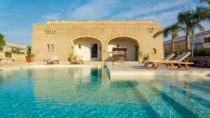 A pool area with lounge chairs and a building with arched doorways. - Relais Tenuta Campì (Martano)